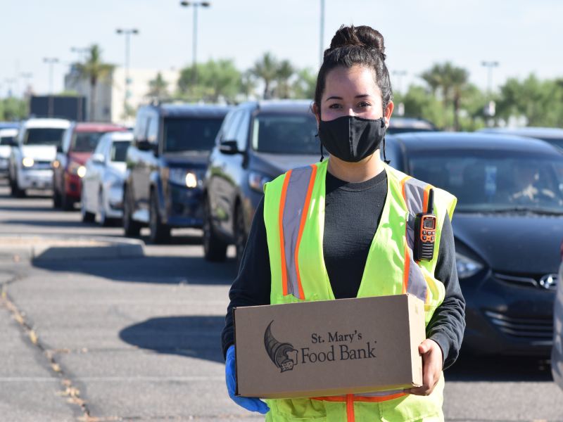 St Mary's Volunteer with Food Box beside Line of Cars
