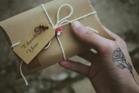 Hand holding a brown paper package with string and a 'Thank You' tag.