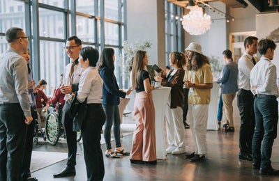 Group of people socializing at a conference in a modern indoor setting with large windows.